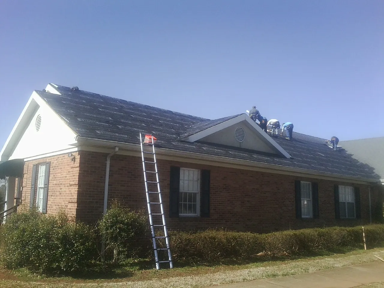 Crew tearing shingles off a brick ranch roof with a ladder set — Emergency Roof Repair work by our crew in Derry