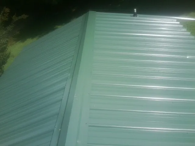 New green metal panels meeting at the ridge of a roof — Flat Roof Repair work by our crew in Derry
