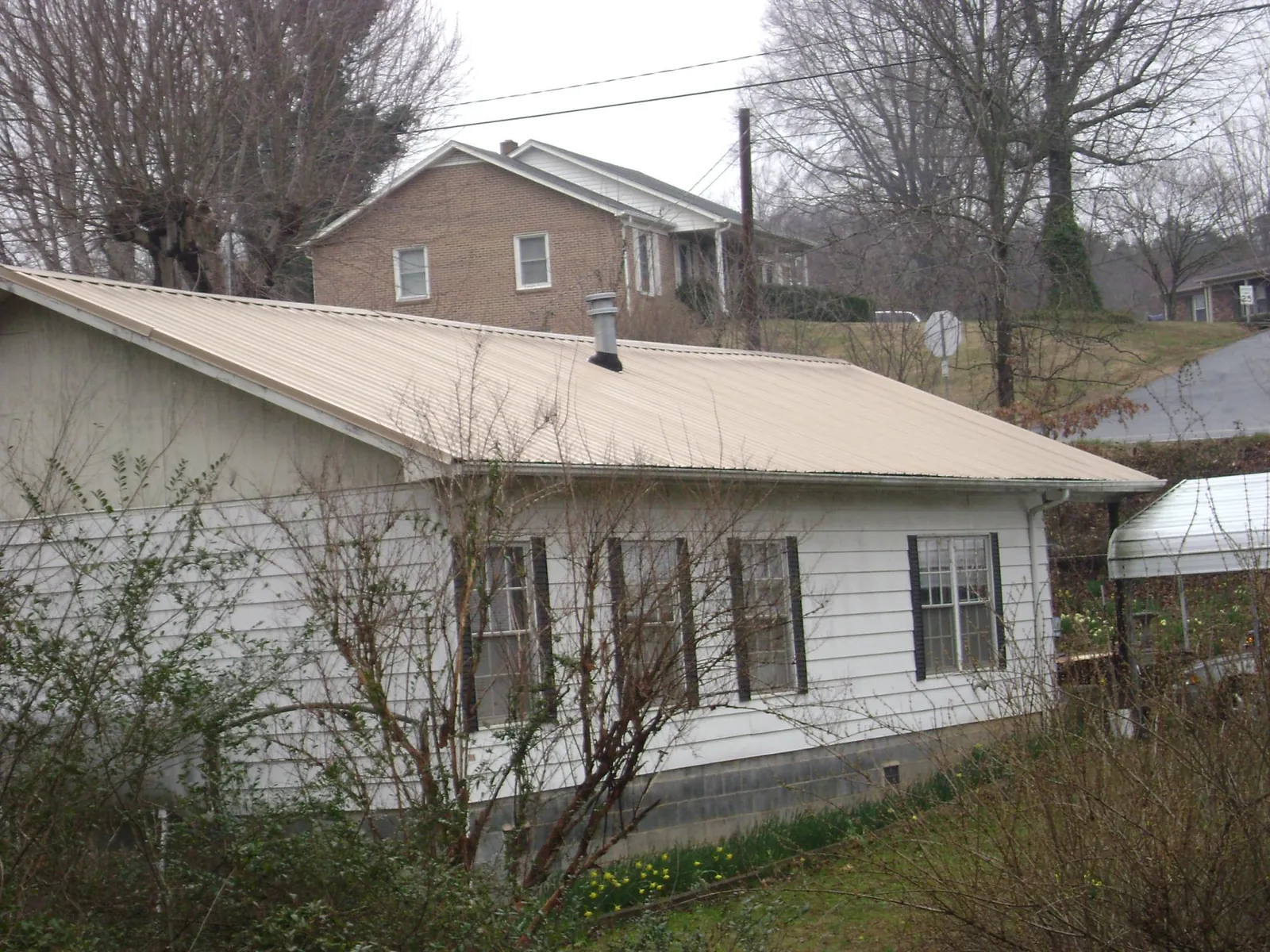 Tan metal roof on a white sided house set into a hillside — Commercial Roofing by Roofing Brothers in Derry